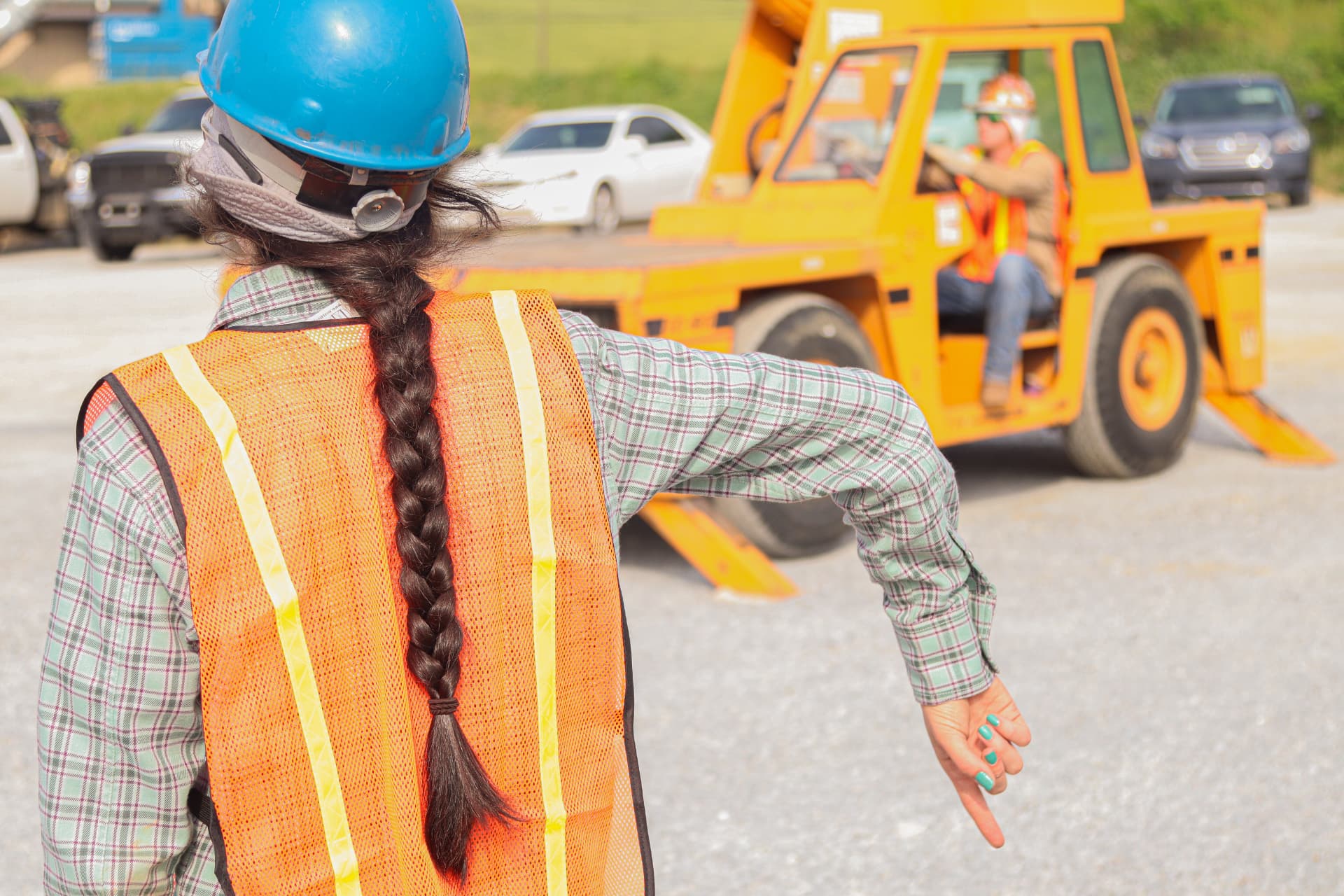 A worker in a hard hat and safety vest signals to a crane operator on an industrial job site