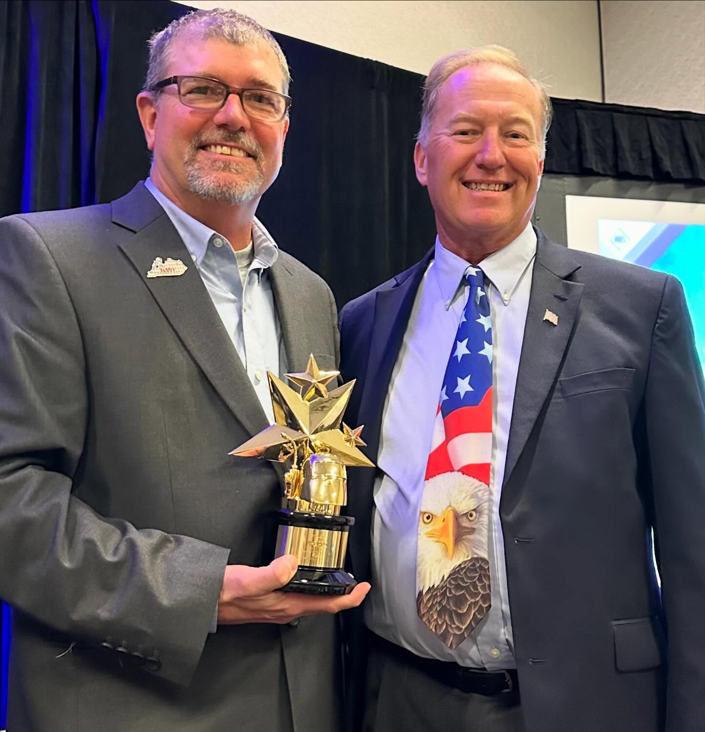 A KWI representative holding a gold AWS award trophy alongside a colleague at an awards ceremony
