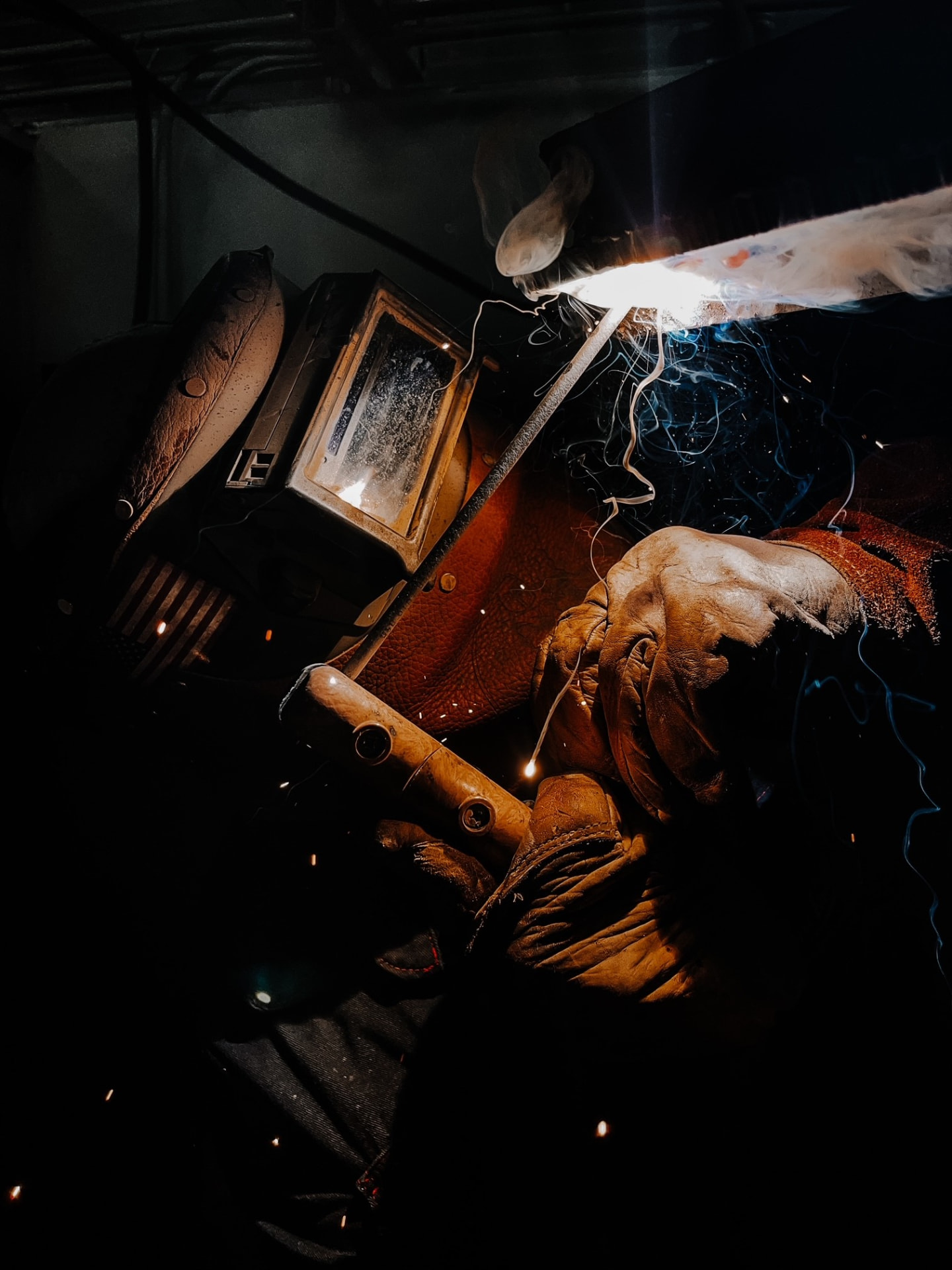 A KWI welder in a leather hood striking a stick arc on structural steel, sparks and smoke rolling off the joint
